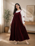 Woman wearing maroon velvet flare maxi dress layered with white bow sleeve inner in elegant indoor setting
