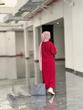 Woman wearing a reddish maroon top and skirt with a pink scarf and checkered bag in a modern indoor setting