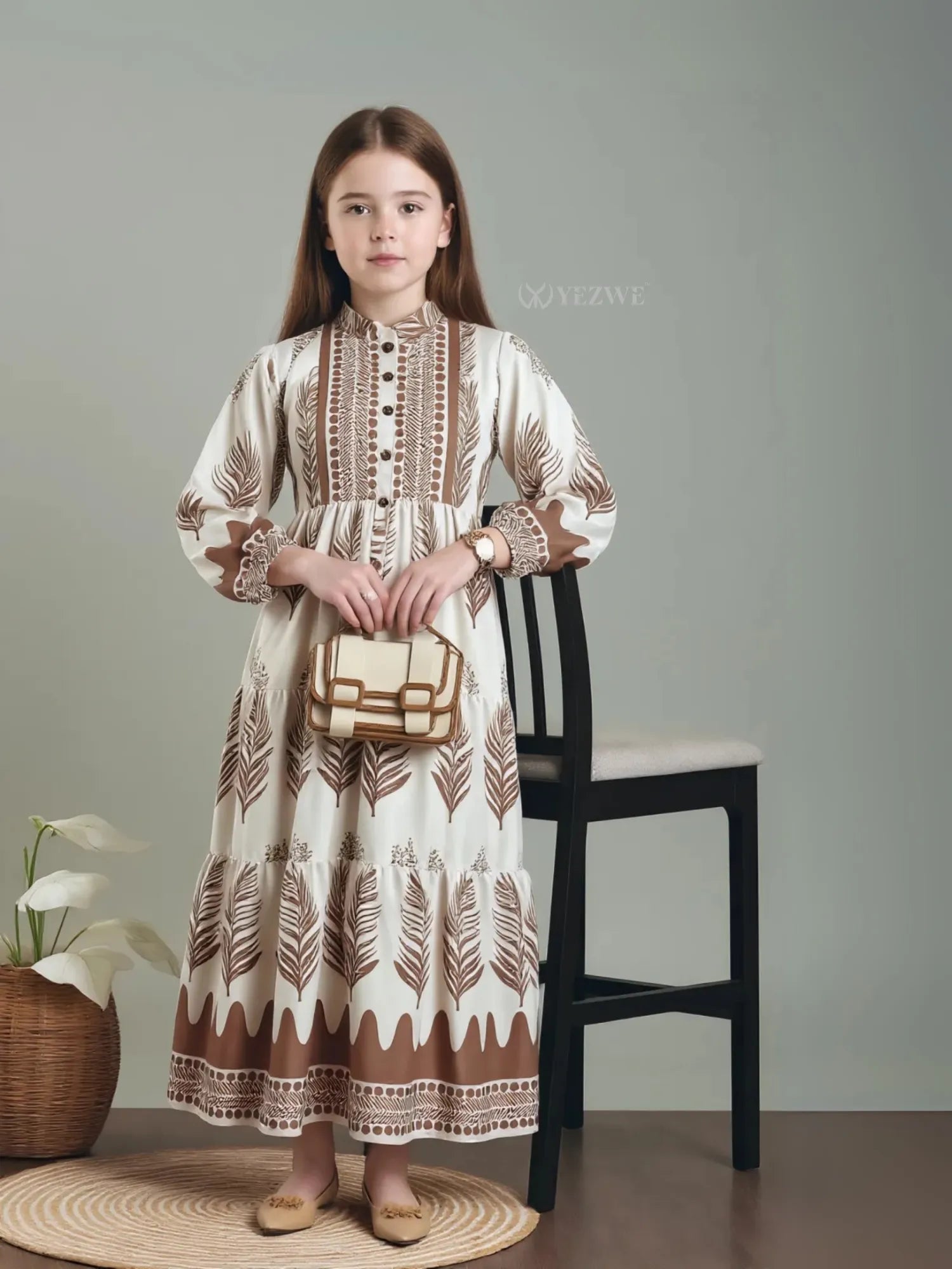 Junior girl wearing a miniature brown feather maxi dress by Yezwe holding a beige handbag