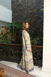 Woman wearing a beige boho print maxi dress with blue paisley detailing standing beside an ornate indoor railing in a modern interior setting.