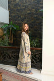 Woman wearing a beige paisley print maxi dress with blue and pastel detailing standing indoors beside a decorative black railing.
