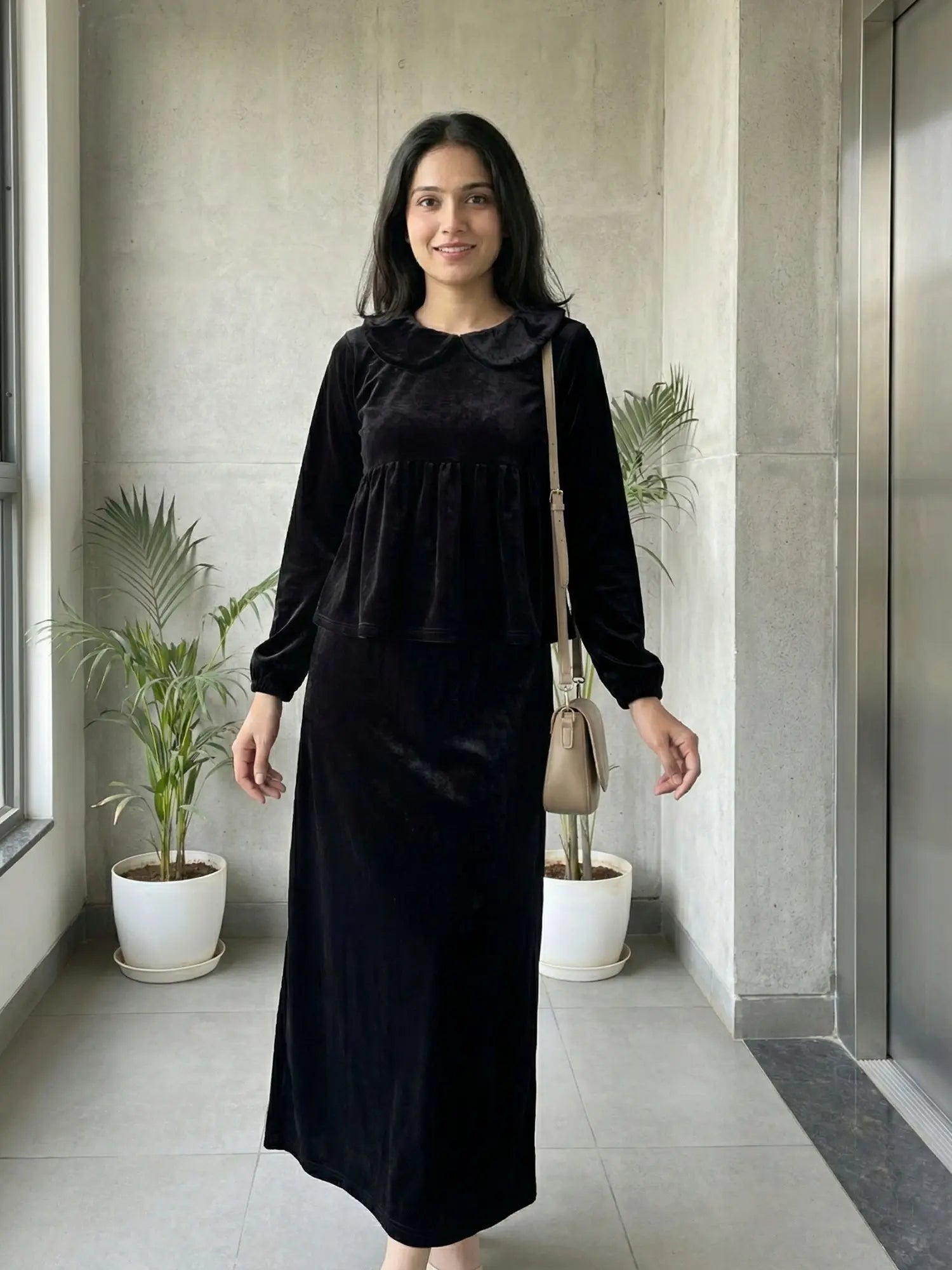 woman wearing black velvet modest maxi dress walking indoors in a clean front view with a crossbody bag