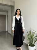 woman wearing black velvet pinafore modest maxi dress with white shirt standing indoors in a slight angled pose