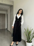 woman wearing black velvet pinafore modest maxi dress with white shirt styled indoors in an elegant pose