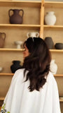back view of woman wearing cream printed modest top indoors with aesthetic shelf background