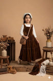 Young girl wearing a brown velvet pinafore dress with white inner top, modest kids outfit in a studio setting