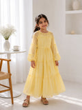 Young girl wearing a pastel yellow tiered maxi dress with puff sleeves and waist tie in a bright minimal indoor setting.
