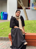 Woman wearing modest black maxi dress by YEZWE sitting outdoors with beige scarf