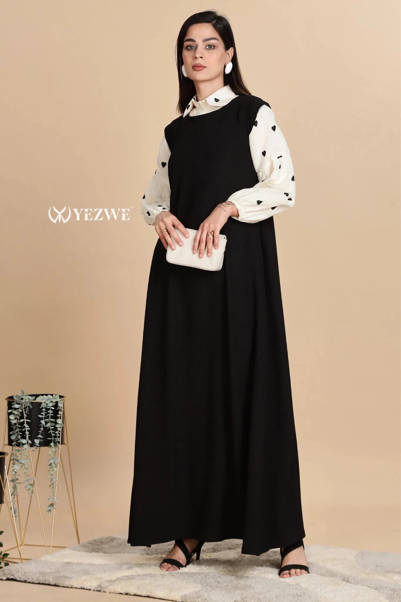 Modest black pinafore dress by YEZWE styled with a white blouse and clutch for a chic look