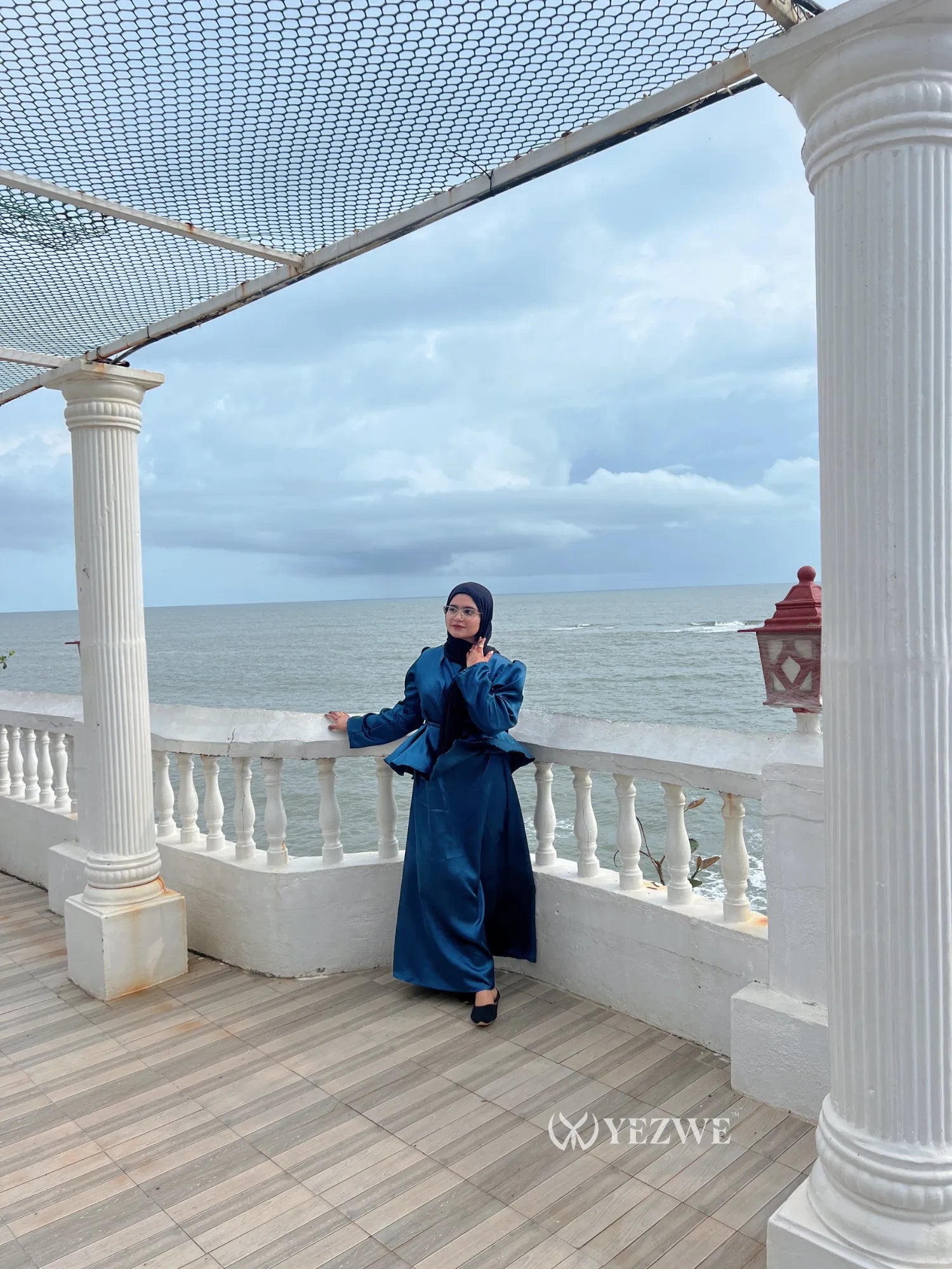 Woman wearing a blue modest co-ord set by YEZWE standing on a terrace overlooking the ocean