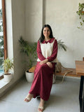 woman wearing wine maroon modest maxi dress with a cream layered sleeveless top sitting indoors in a relaxed lifestyle pose