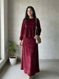 woman wearing wine maroon velvet modest maxi dress standing indoors with a crossbody bag front view