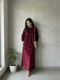 woman wearing wine maroon velvet modest maxi dress standing indoors in a relaxed lifestyle pose with a crossbody bag