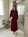 woman wearing wine maroon velvet modest maxi dress walking indoors with a crossbody bag in a lifestyle setting