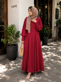 Woman wearing a maroon modest maxi dress with puff sleeves and beige hijab standing outdoors near a café.