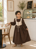 Junior girl wearing a brown full-length maxi dress with cream corset-style bodice and puff sleeves in a cozy café setting.
