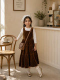 Junior girl wearing brown velvet layered pinafore dress with white inner top in cozy cafe setting