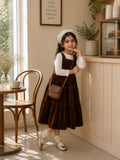 Junior girl wearing brown velvet tiered pinafore dress with white full sleeve inner top and sling bag