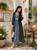 Woman wearing a modest green velvet and blue patterned maxi dress with long sleeves, standing in an elegant outdoor café setting with a vintage aesthetic.