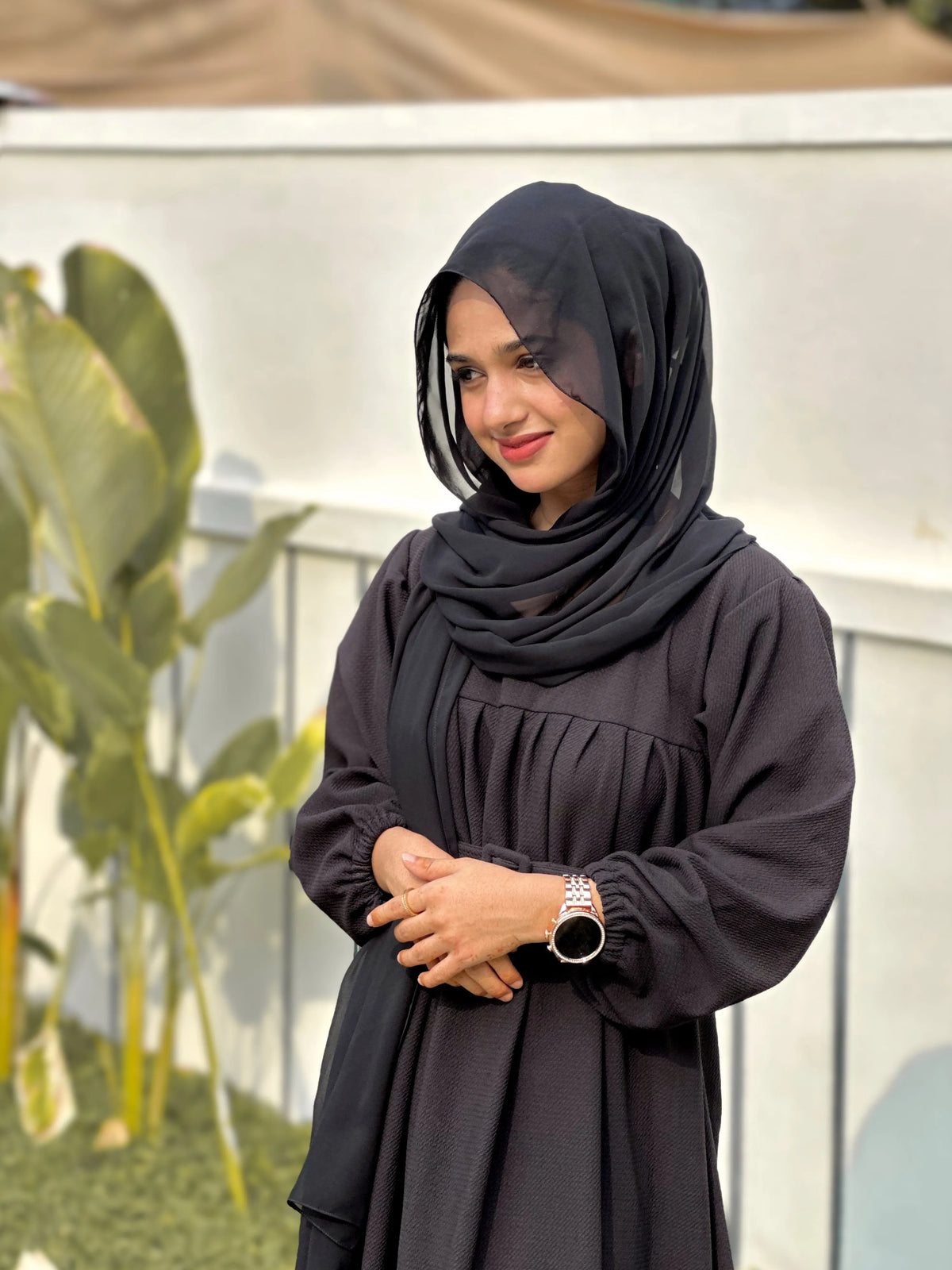 Woman in a Black Textured Maxi Dress with long sleeves and a stylish hijab against a garden backdrop