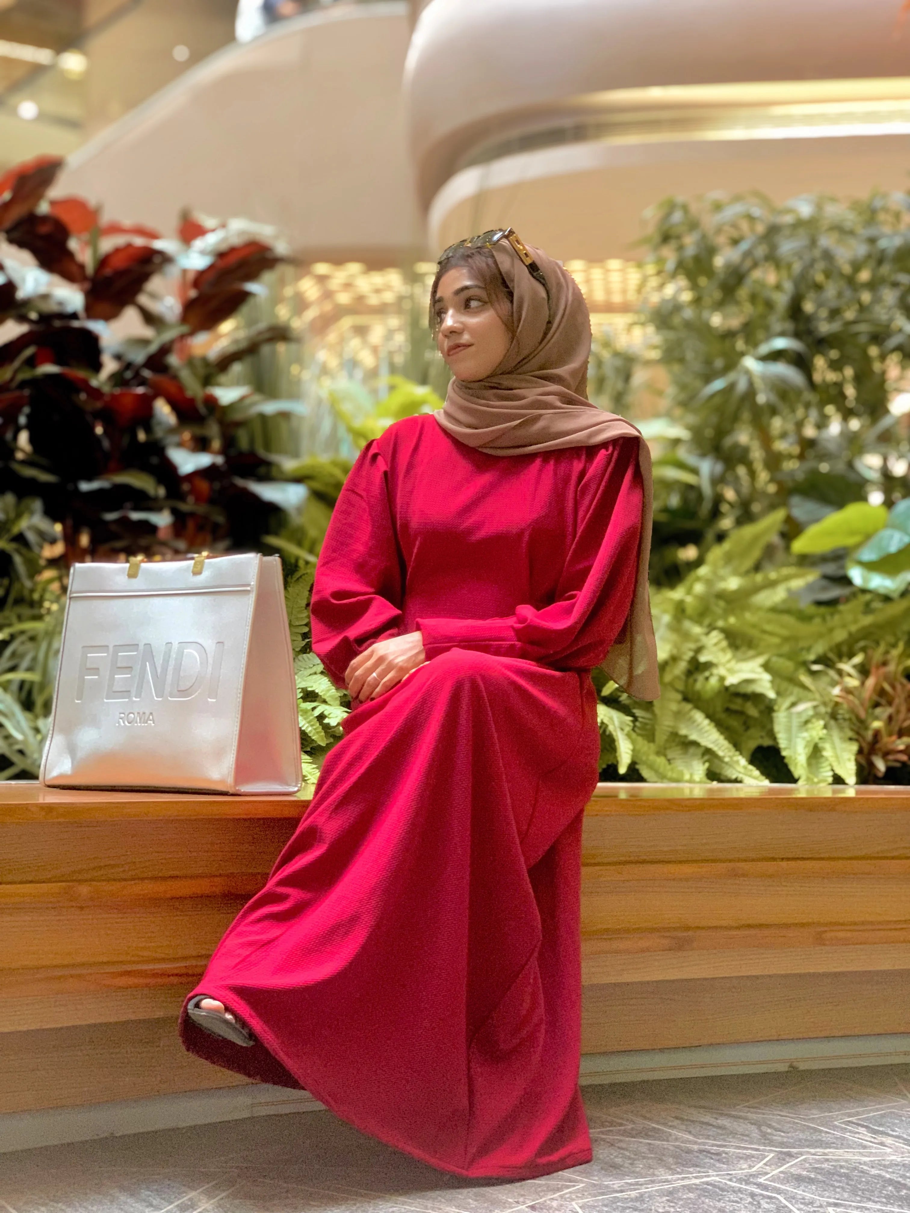 Yezwe knitted Modest maxi dress for women in vibrant red, styled with a headscarf and sitting in a lush indoor setting