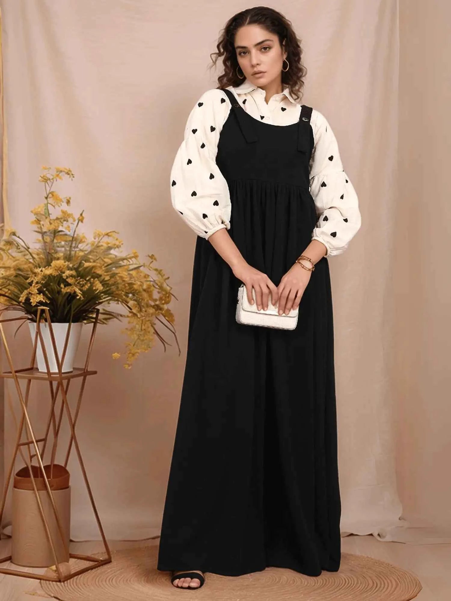Elegant model wearing a modest black and white pinafore over a patterned blouse, styled with accessories