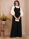Elegant model wearing a modest black and white pinafore over a patterned blouse, styled with accessories