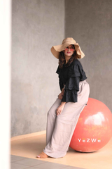 Chic woman in a modest black co-ord set with ruffled sleeves and wide-leg pants, wearing a sun hat and sunglasses