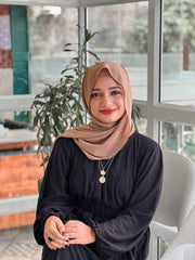 Woman in a modest black maxi dress with a hijab, sitting in a bright indoor setting