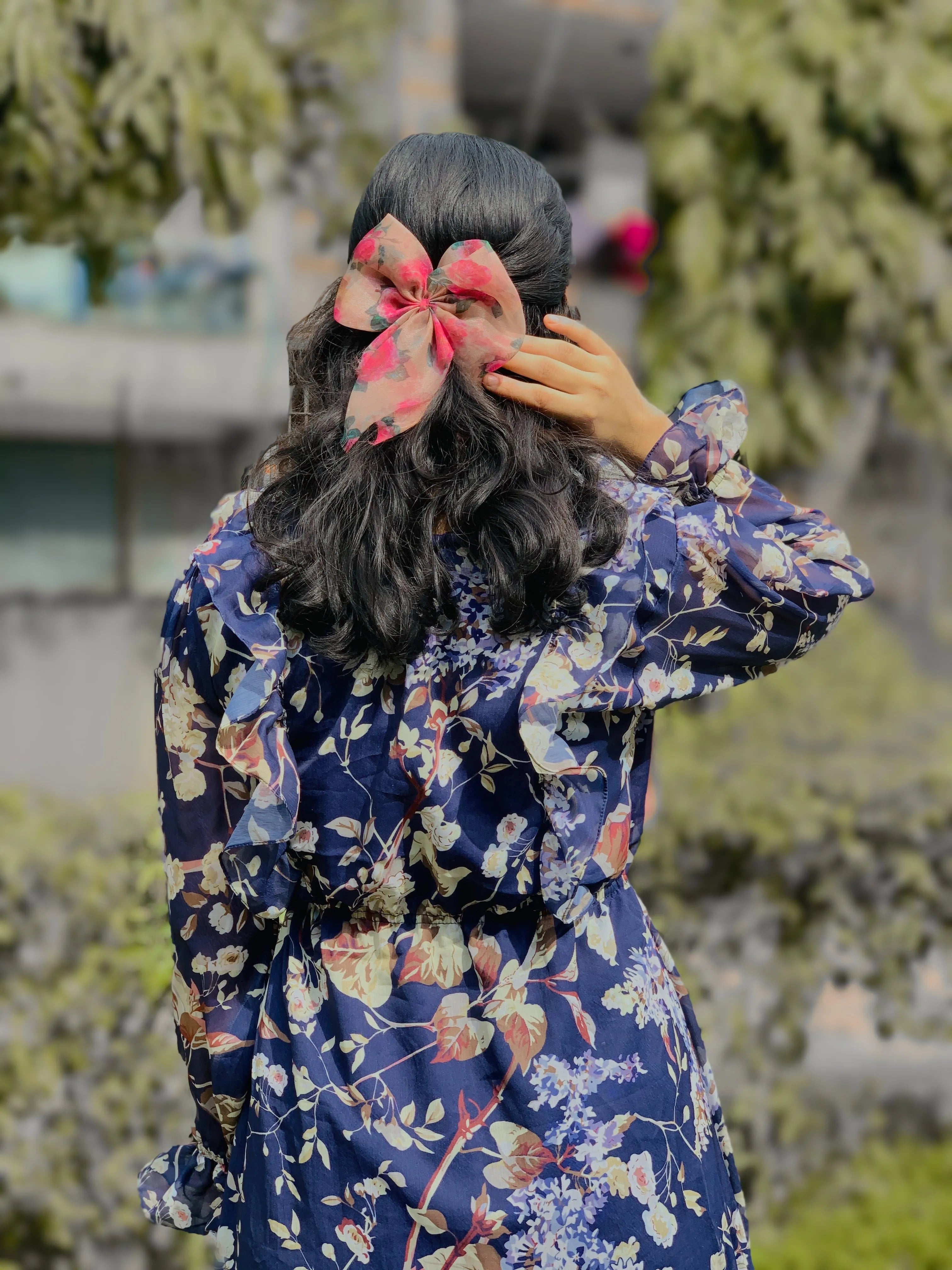 Back view of a woman wearing a modest floral georgette maxi dress with a bow in her hair
