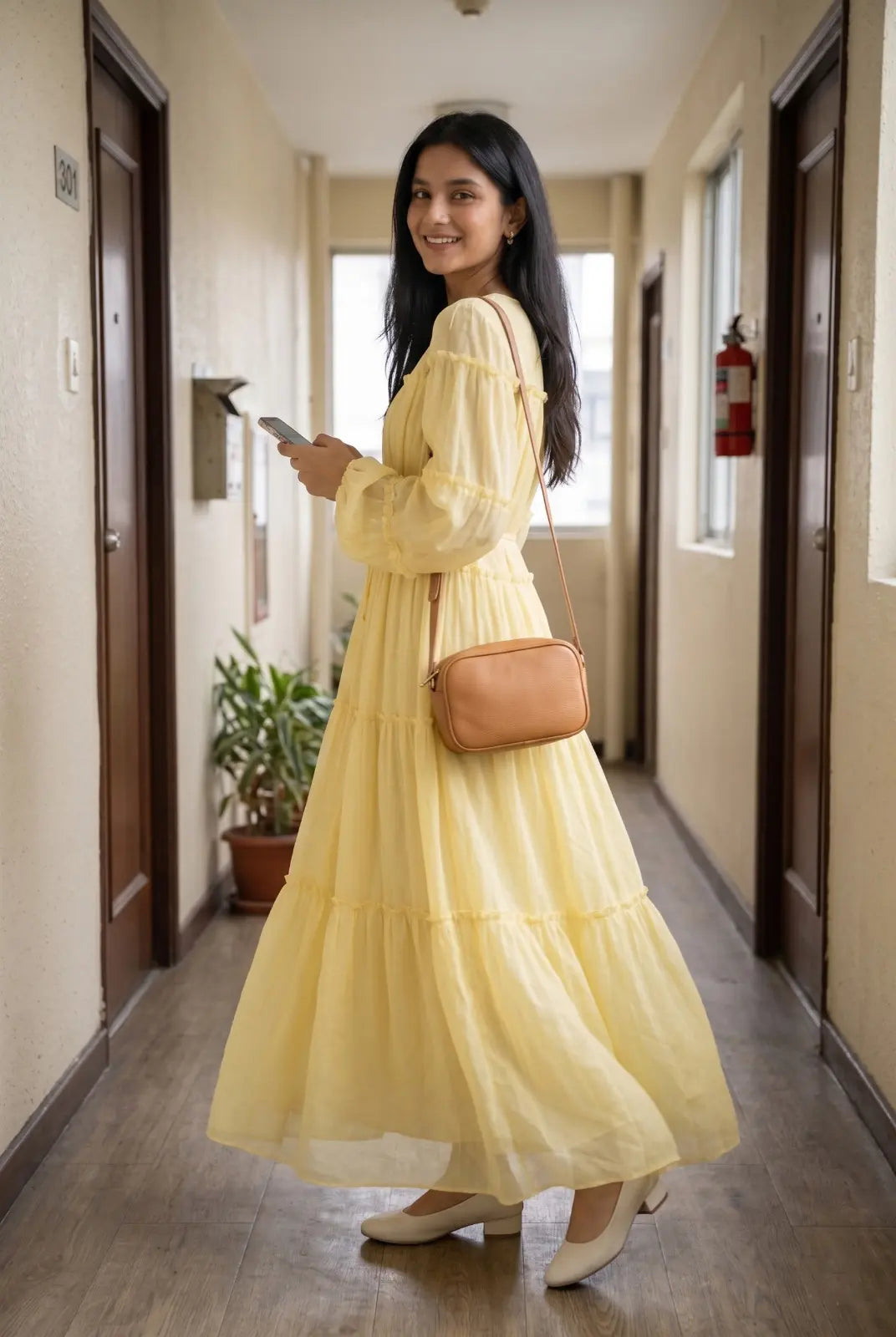 Woman walking indoors wearing a pastel yellow tiered maxi dress with flowy silhouette, modest Pinterest style outfit with sling bag