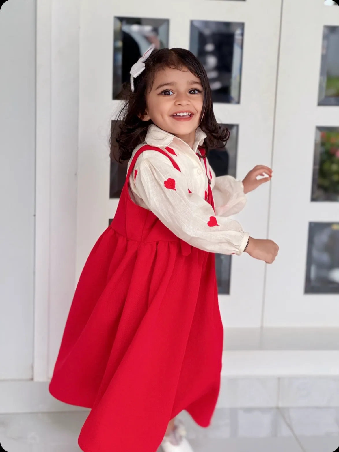 Smiling young girl wearing a red pinafore for junior girls over a white blouse with red hearts