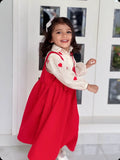 Smiling young girl wearing a red pinafore for junior girls over a white blouse with red hearts