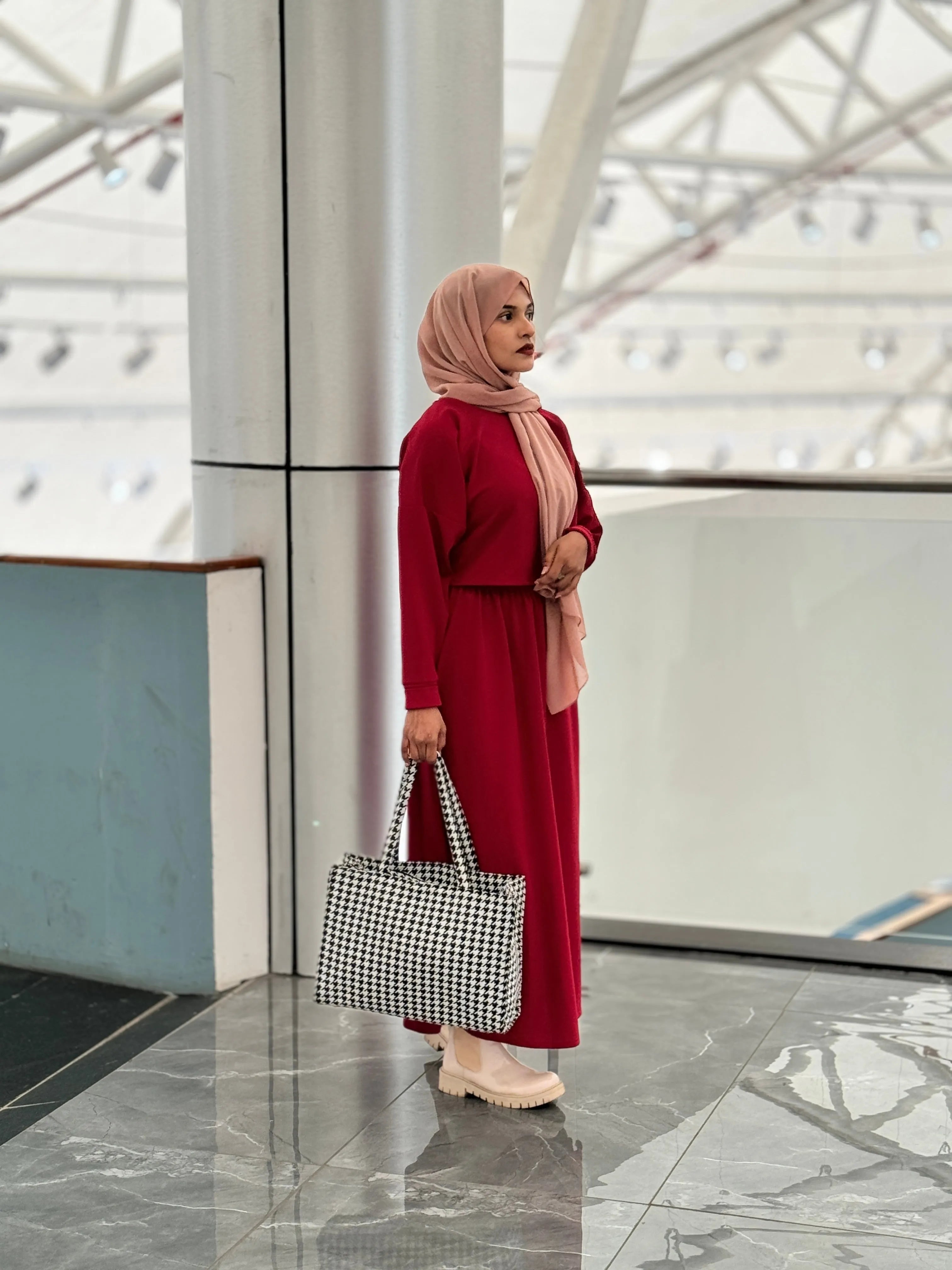 Stylish woman in a reddish maroon top and skirt, accessorized with a scarf and a checkered handbag
