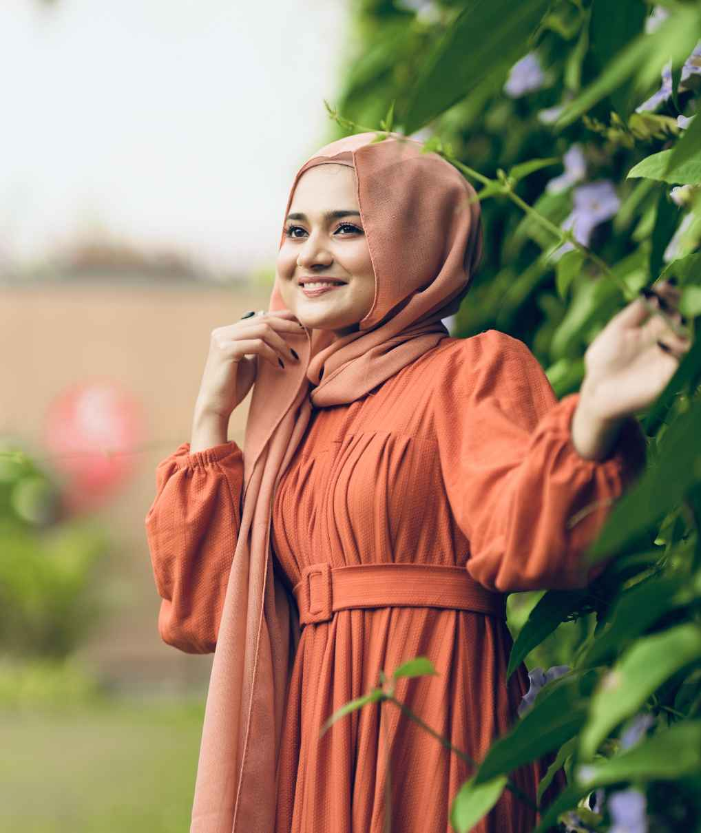 Woman in a textured rib maxi dress with belt posing among green plants and smiling