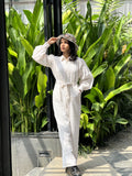 Model wearing a stylish white textured jumpsuit with a belted waist in a tropical setting