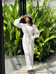 Model wearing a stylish white textured jumpsuit with a belted waist in a tropical setting