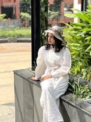 Model wearing a white textured jumpsuit from Yezwe, styled with a fashionable hat in a garden setting