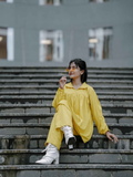 Stylish woman sitting on steps in a yellow oversized co-ord set with chic silver boots
