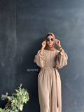 Woman wearing YEZWE Nomade Cey Jumpsuit with a hijab and sunglasses standing at glass door entrance