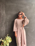 Woman wearing YEZWE Nomade Cey Jumpsuit with a hijab and sunglasses standing at glass door