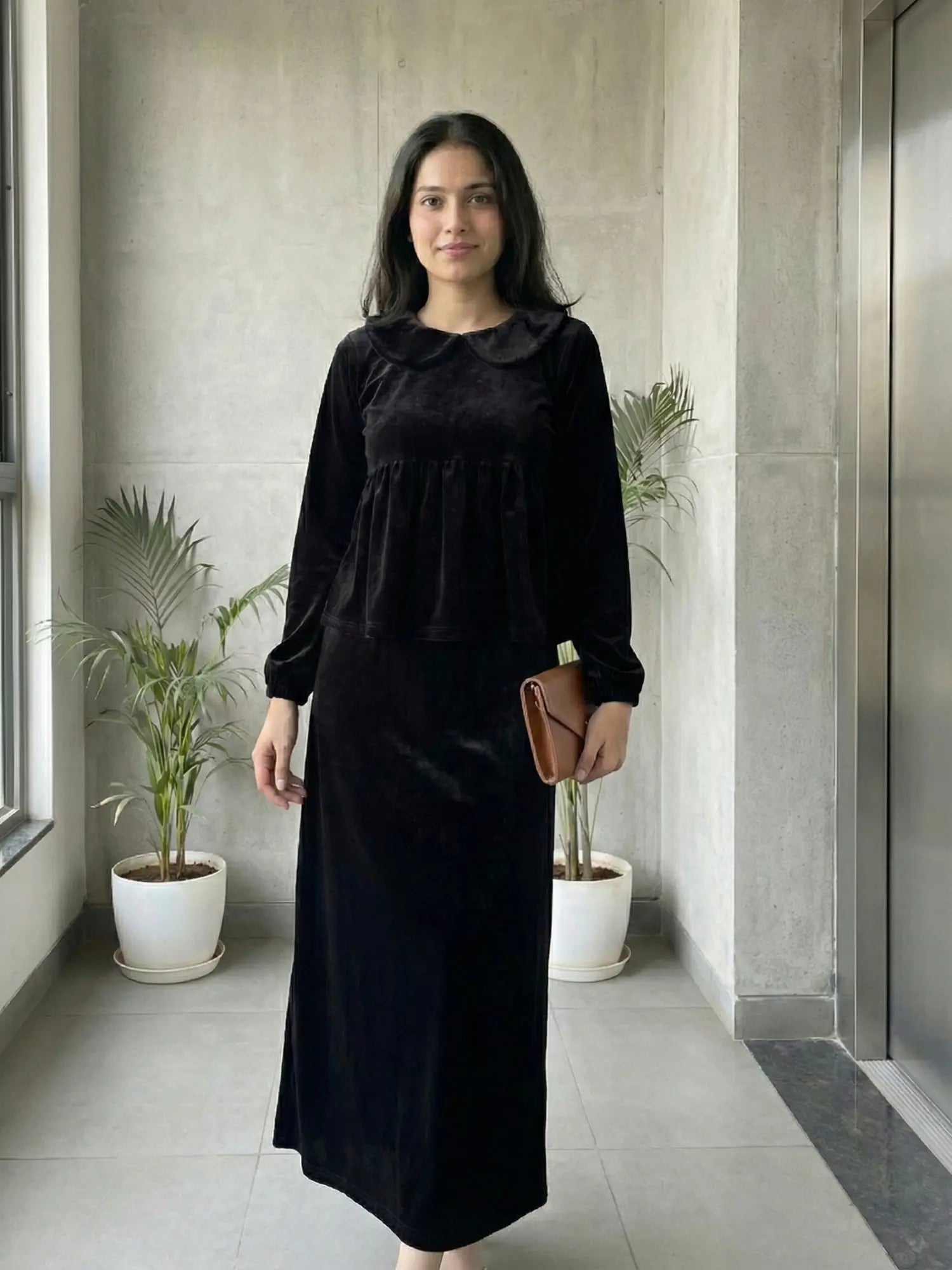 woman wearing black velvet modest maxi dress standing indoors holding a small clutch