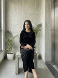 woman wearing black velvet modest maxi dress sitting indoors holding a clutch in a relaxed lifestyle pose