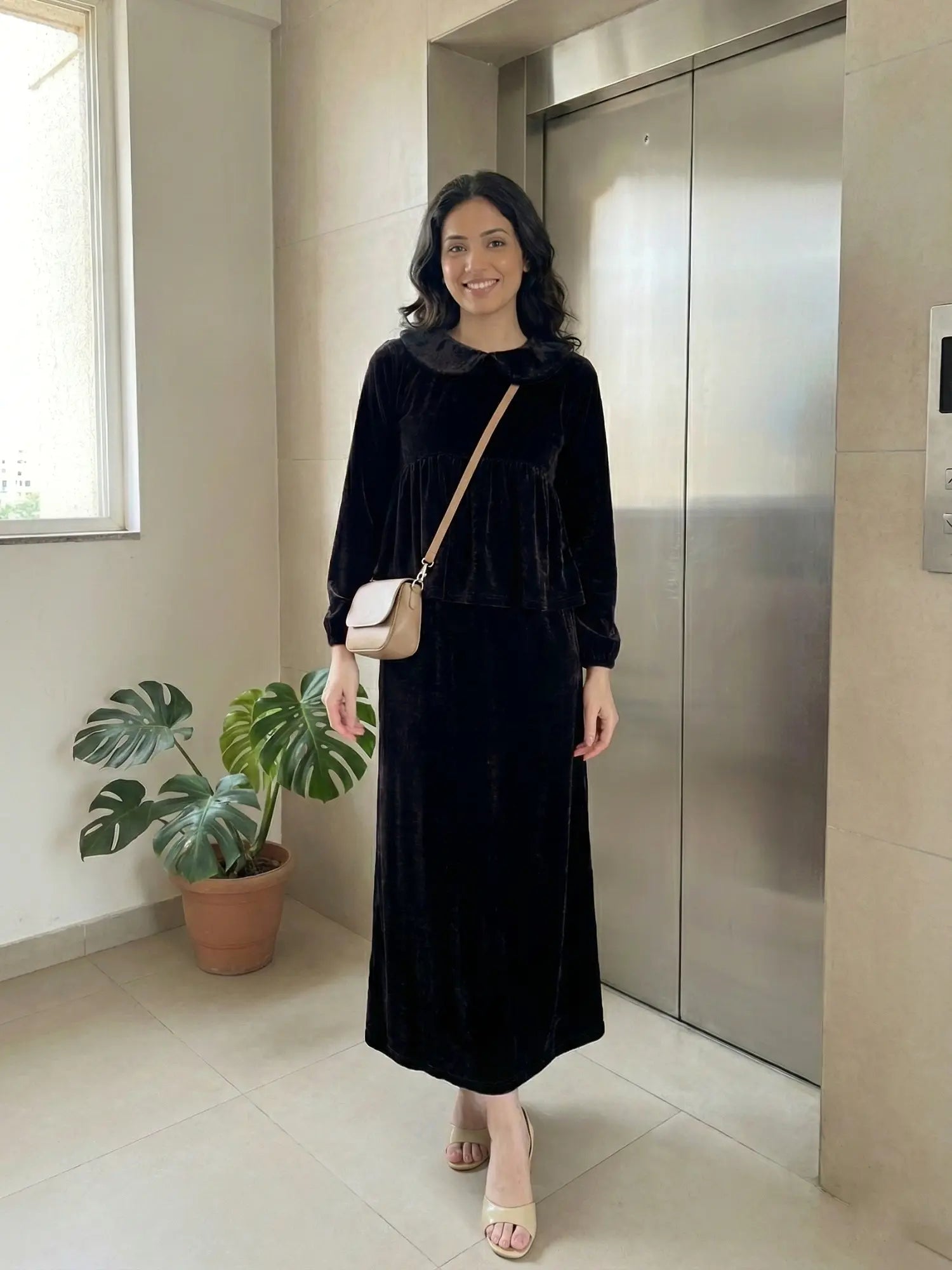 woman wearing black velvet modest maxi dress walking indoors with a crossbody bag in a stylish pose