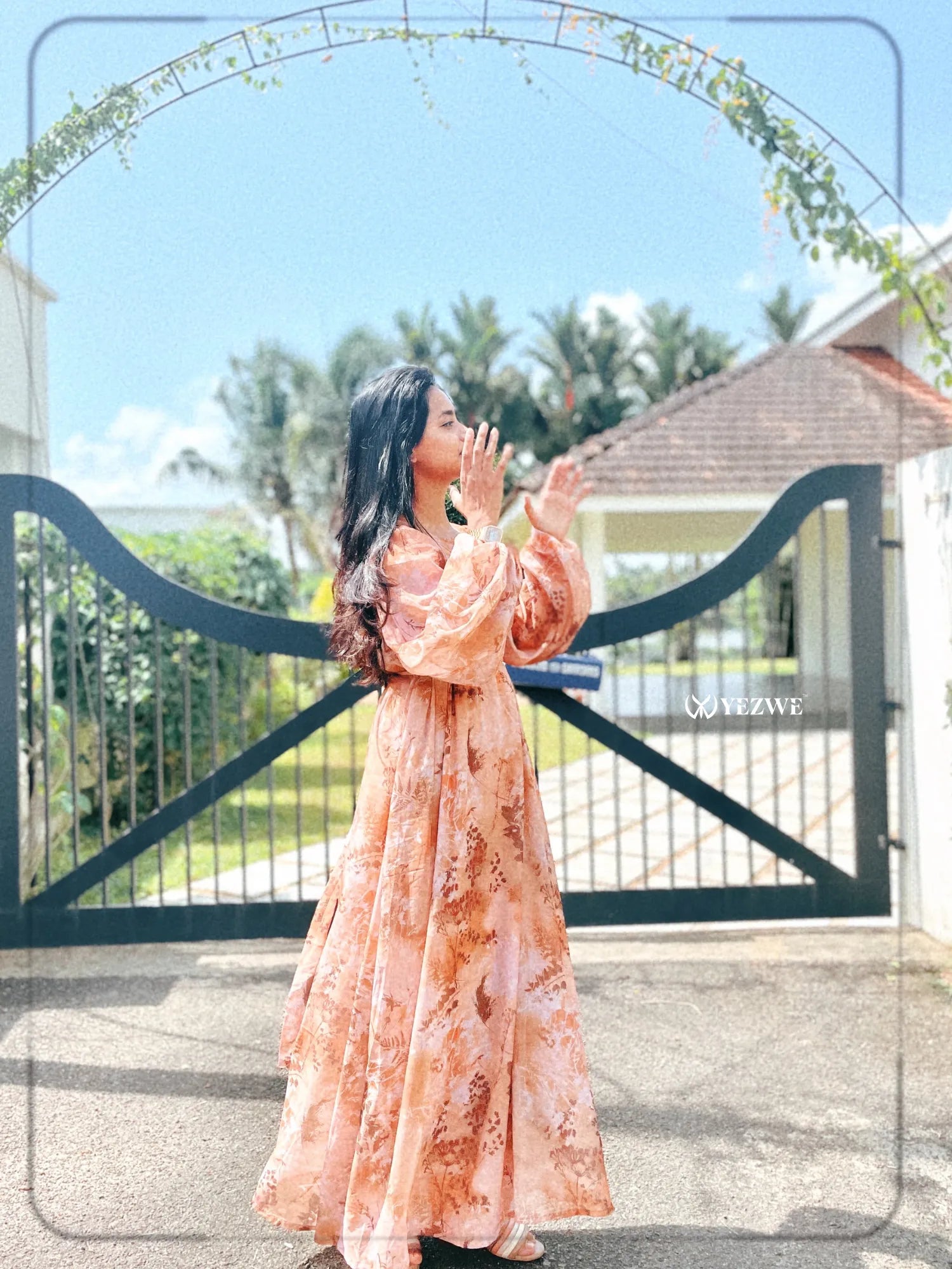 Model wearing a brown floral georgette maxi dress, showcasing a flowy design in a sunny outdoor setting