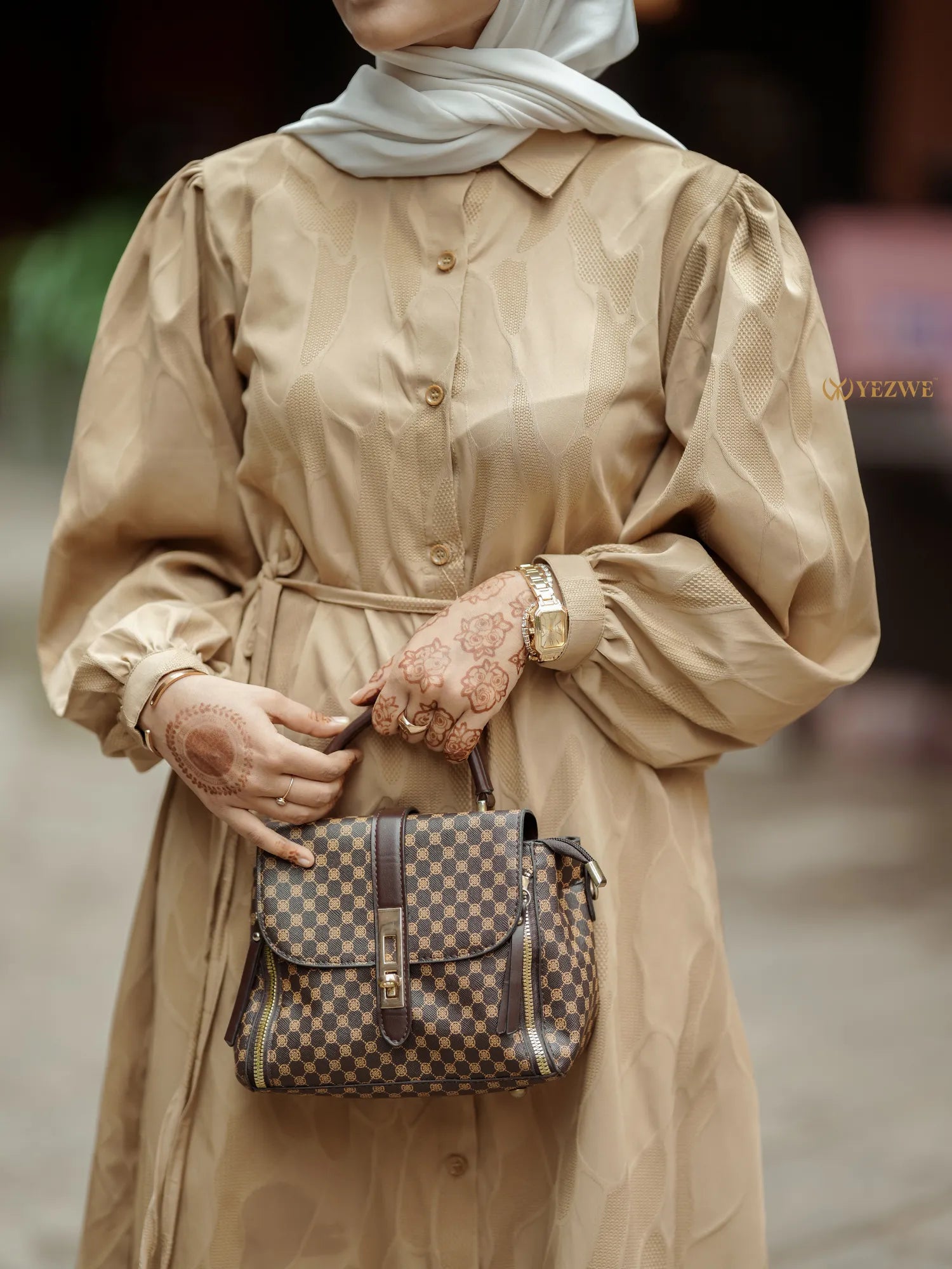 Elegant brown textured maxi dress with long sleeves and a cinched waist, paired with a stylish handbag
