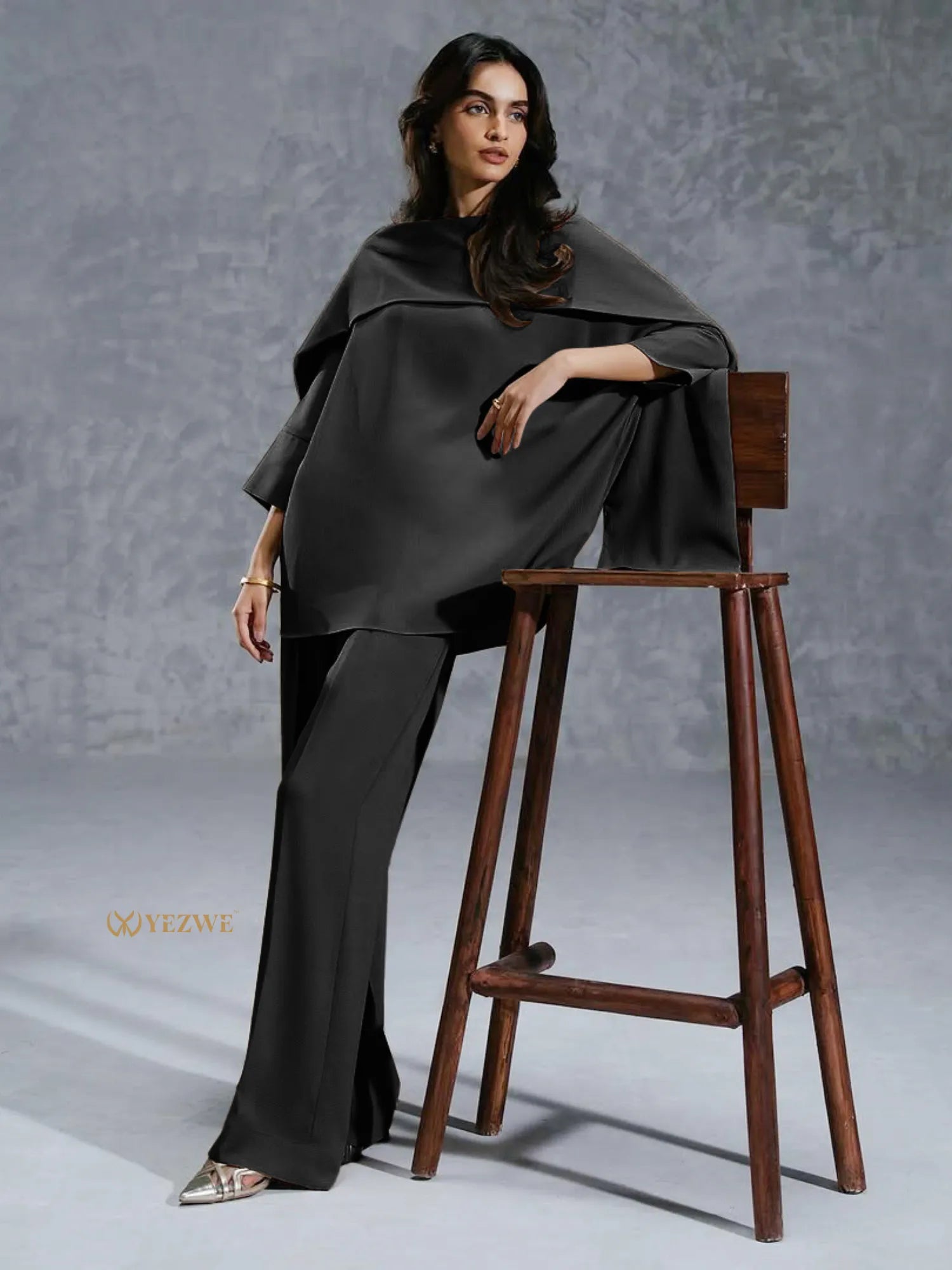 YEZWE black co-ord set featuring a loose top and wide-leg pants worn by a woman leaning on a wooden stool