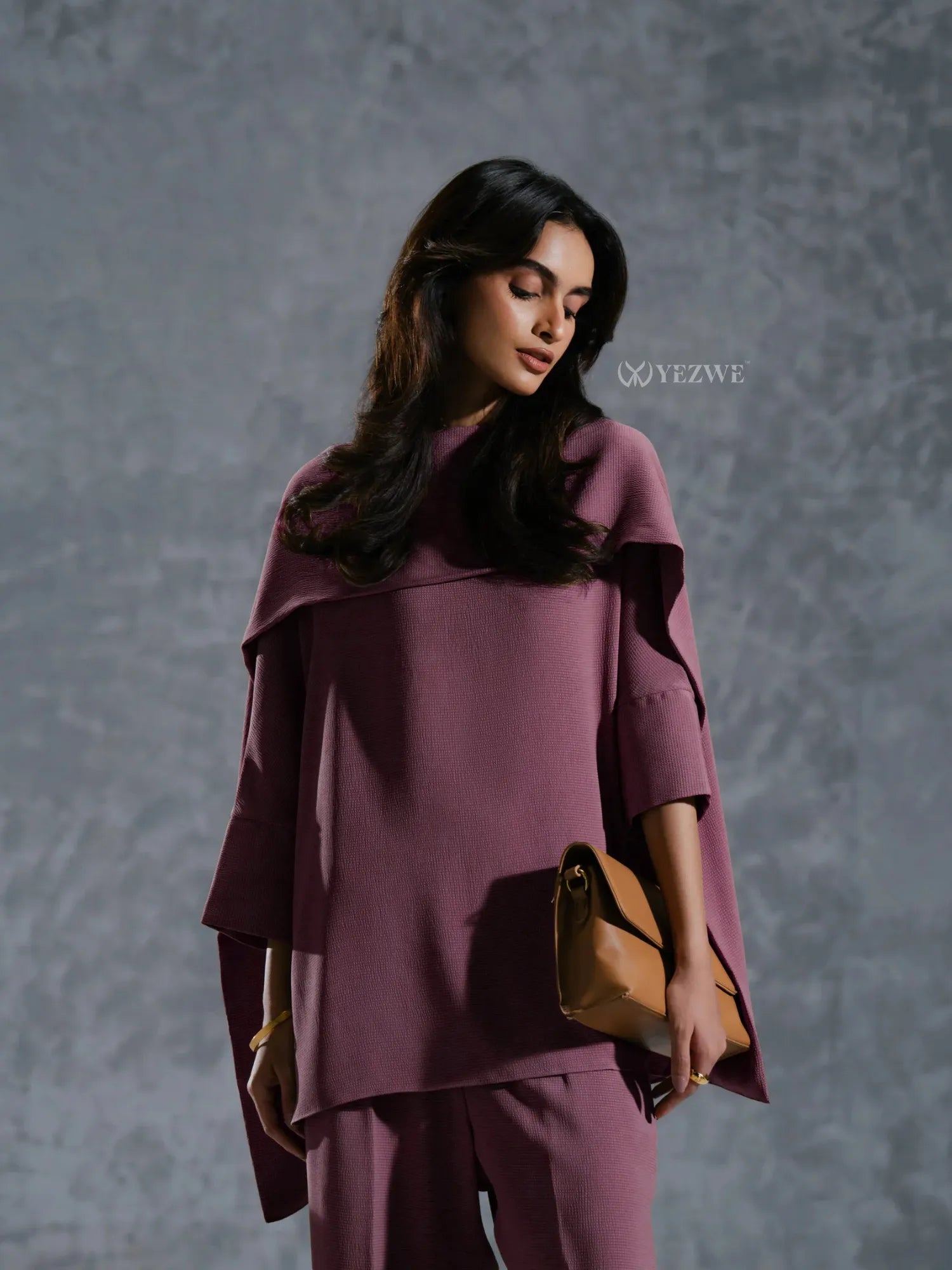 Woman wearing a mauve YEZWE Co-Ord Set with long sleeves holding a tan clutch bag