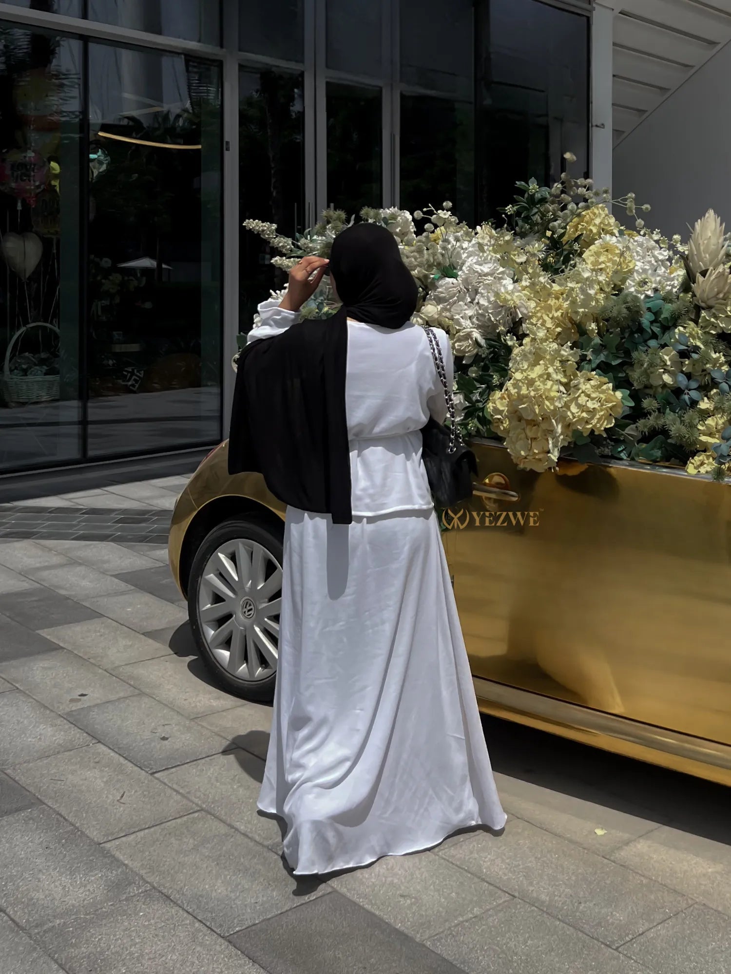 YEZWE white Co-Ord set with long skirt and blouse worn with black hijab outdoors near golden flower planter