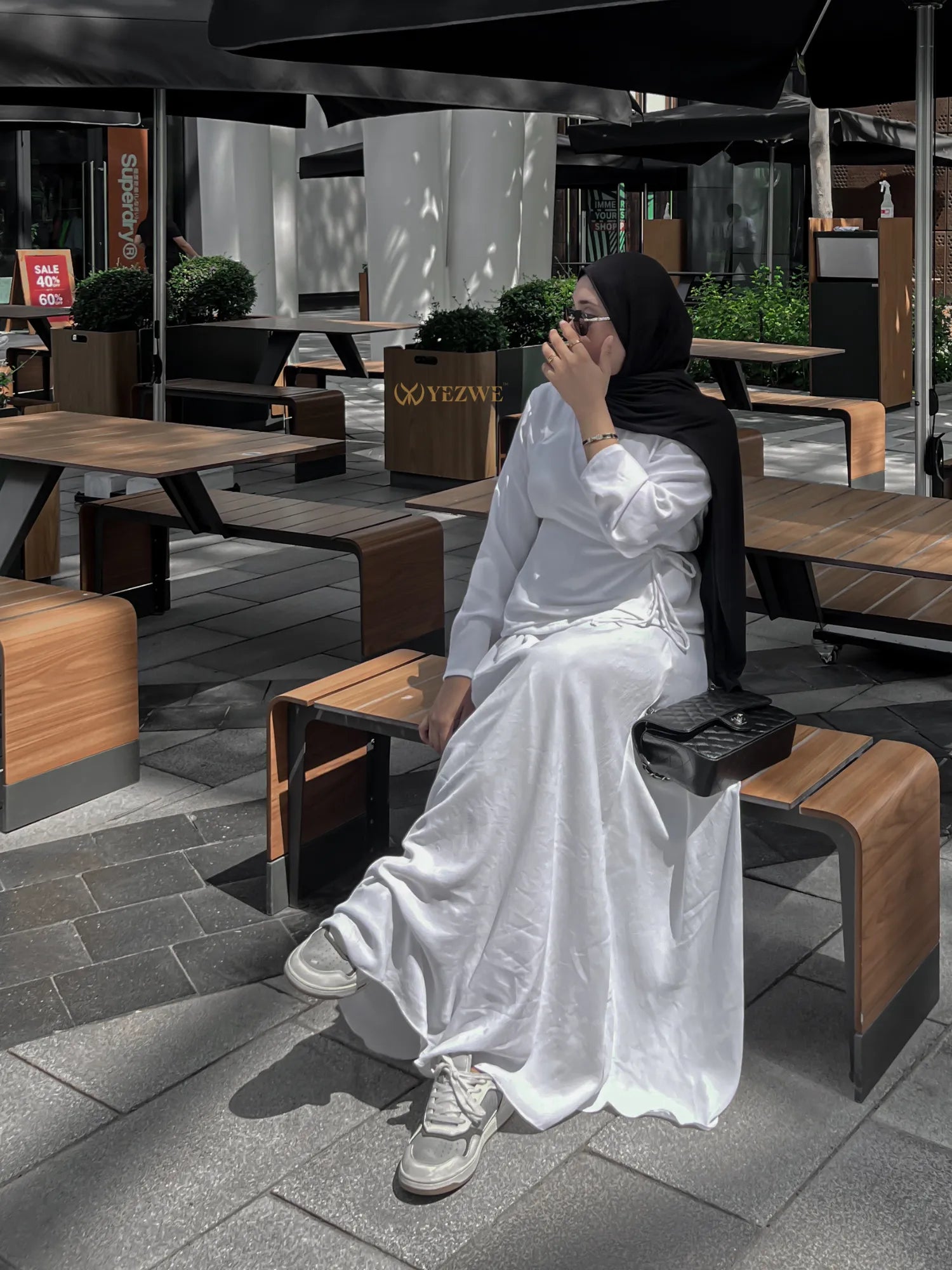 Woman wearing white YEZWE Co-Ord set with long skirt and hijab sitting outdoors on wooden bench